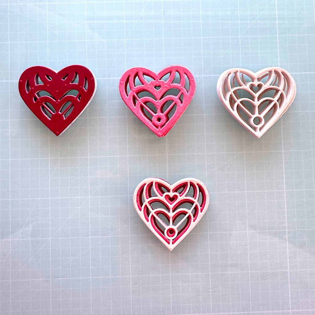 Four stacks of heart die cuts. The first one is darkest and has the largest surface area. The next one is medium in both tone and surface area etc. The last one consists of one heart from each of the previous stacks. It creates a visually appealing stylized heart in three tones. 