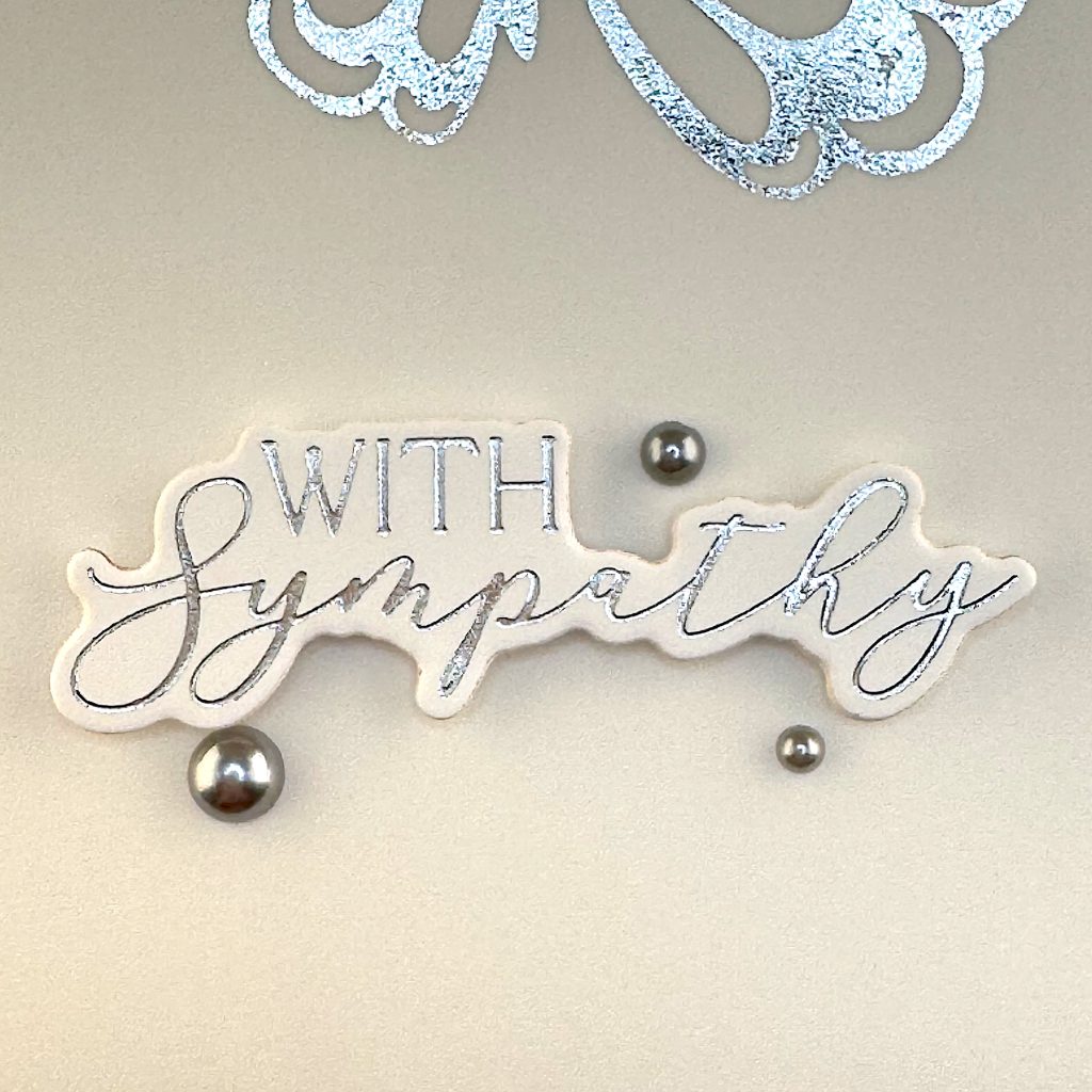 Detail of greeting card showing the greeting "With Sympathy" surrounded by three matte, silver pearls of different sizes.