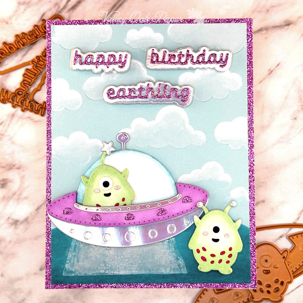 Greeting card with a sky blue background. A little green alien sits in a flying saucer and another one stands on the ground outside it. The greeting reads "Happy birthday Earthling." 