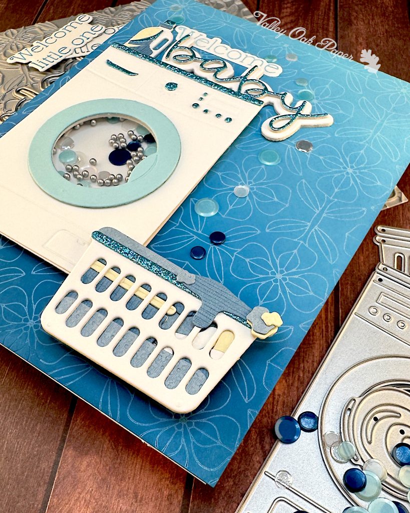 This view of the Welcome Baby card emphasizes the dimension of the laundry basket and the bubbles next to the washing machine. 