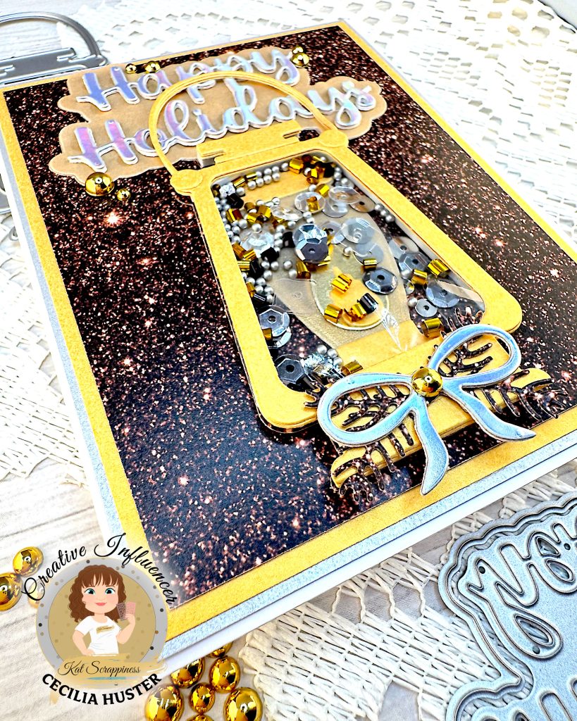Greeting card in gold and silver tones. The main feature is a gold lantern with many gold and silver sequins inside. The large greeting reads "Happy Holidays." In the foreground some flat back gold pearls are visible.