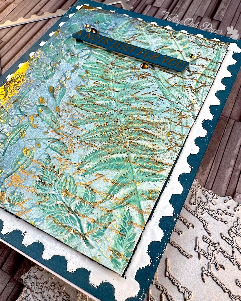 Viewing the card at an angle causes the imprint of various leaves and ferns in green to be emphasised.