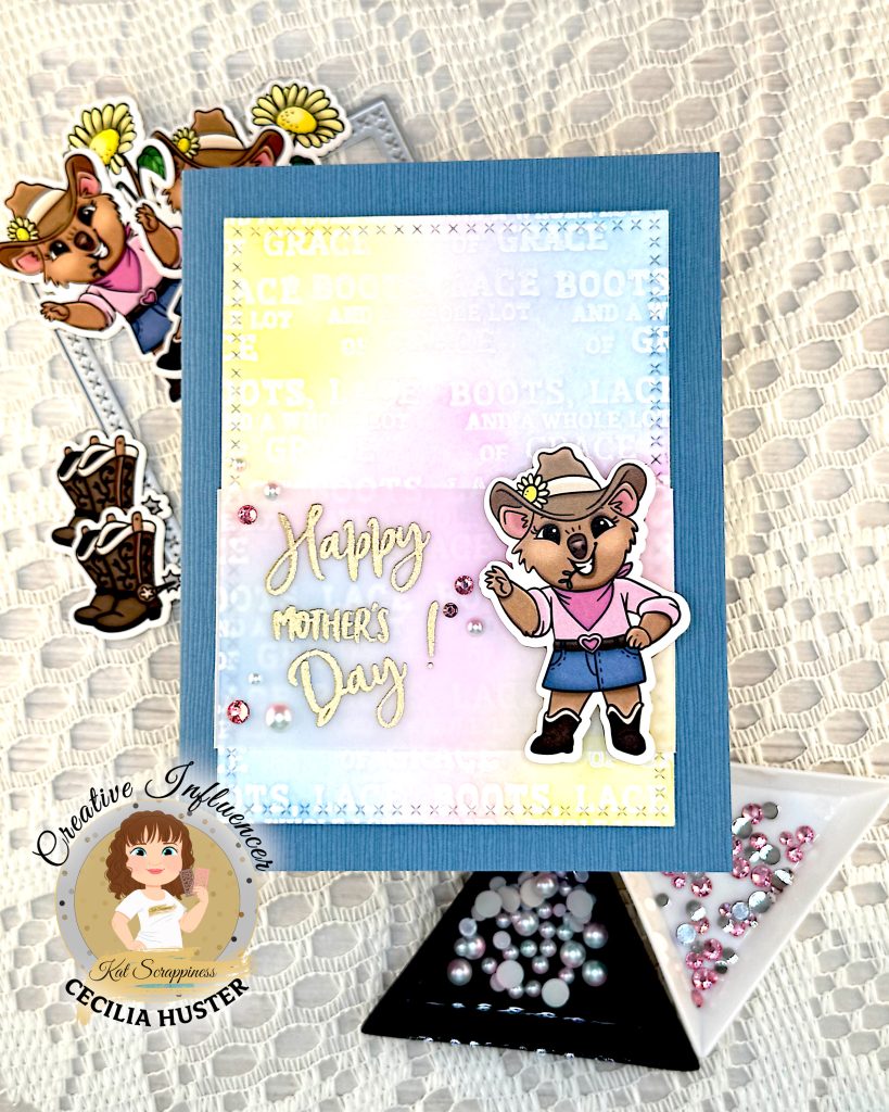 Denim blue greeting card with a background in pastel colors. The focal point is a cowgirl quokka next to the sentiment. The sentiment reads "Happy Mother's Day!"
The card is lying on some white lace with more cowgirl ephemera under it.