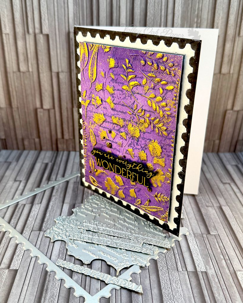 A black greeting card seen from an angle. A purple postage stamp is taking up most of the space. The greeting reads "You are everything wonderful." The card is standing on some of the press plates used to create it.