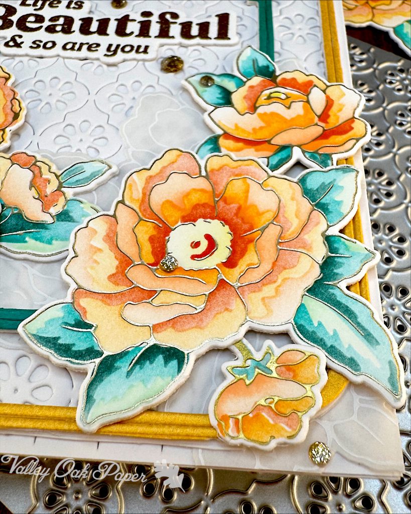 Detail from a white greeting card. The main focus is a large flower in orange and yellow tones with teal leaves. It's placed on two thin frames, one dark teal and one yellow. A white-on-white floral motif is layered under the frames but on top of a stylized daisy pattern motif.