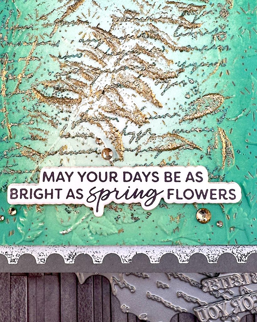 On a grey background lies a grey greeting card. In this shot the greeting is the main star. It reads "May your days be as bright as spring flowers." Under the card some of the press plates used to create it are peeking out.