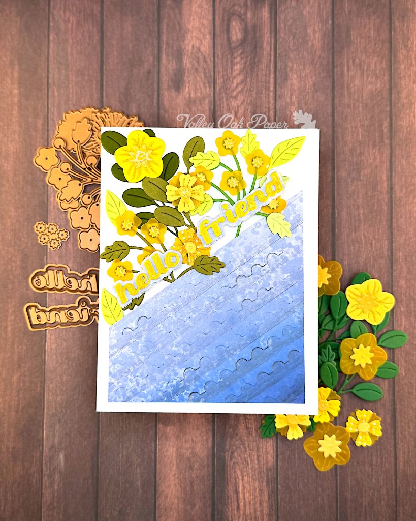 White greeting card with half of the surface a blue gradient embossed with a postage stamp edge design. The other half is a mix of flowers and foliage in yellow and green tones. The sentiment reads "Hello Friend."
Under the card some more flowers can be seen, as well as some of the dies used.