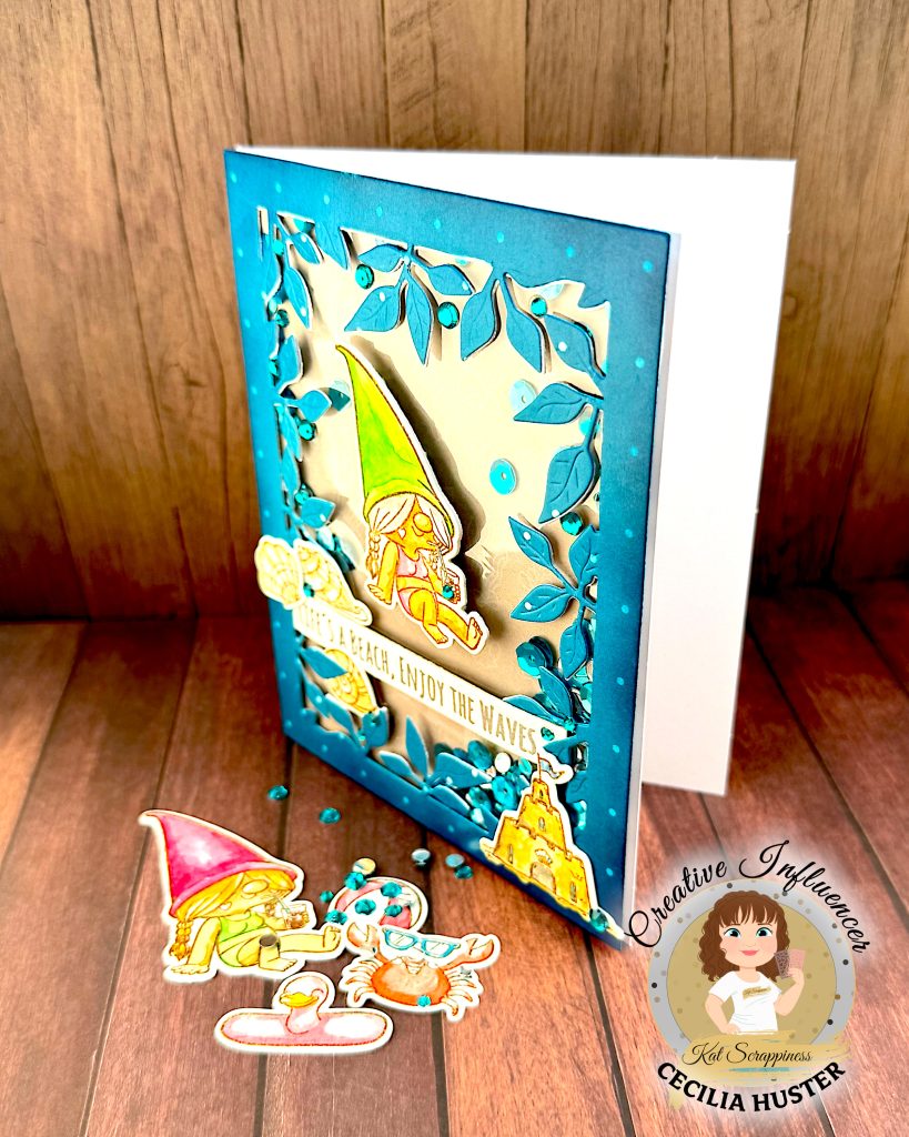 A handmade greeting card with a beach gnome theme displayed on a wooden surface. The card features a clear window filled with turquoise and silver sequins. The window is bordered by a teal, leafy frame.
The main design shows a cute gnome with long, grey hair and a bright green pointed hat. She appears to be relaxing in a bikini while holding a small drink. A banner across the card reads "LIFE'S A BEACH, ENJOY THE WAVES!" The banner is decorated with sea shells. A sandcastle has been placed in the lower right corner.
In front of the card are several coordinating die-cut elements including another gnome figure with a pink hat, a pink flamingo pool floatie, and turquoise gems scattered around. The bottom right corner shows the "Kat Scrappiness Creative Influencer CECILIA HUSTER" logo featuring a cartoon woman with brown hair.