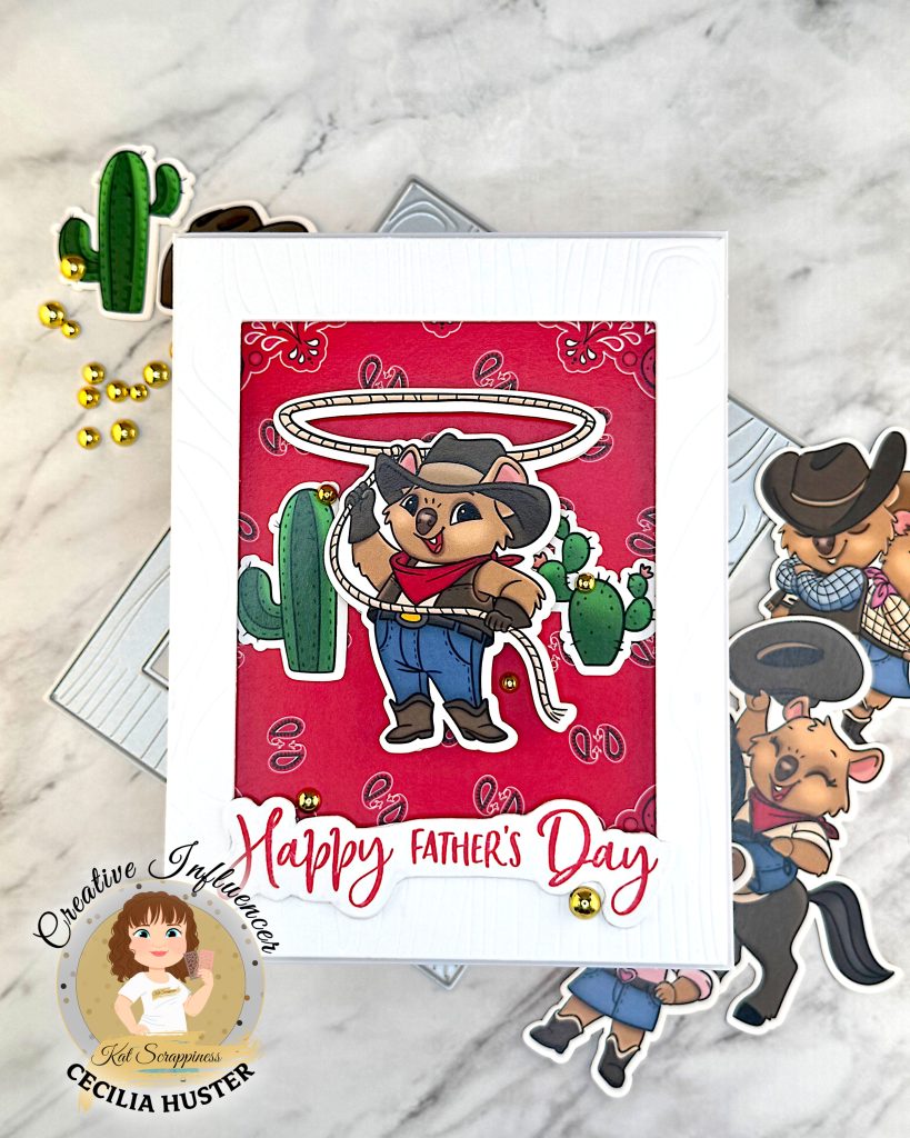 A Father's Day greeting card featuring a cute cartoon cowboy quokka character wearing a black cowboy hat, red bandana, and blue overalls. He is twirling a lasso with cacti in the background. The card has a red patterned background and "Happy Father's Day" text in red script lettering.
The scene is photographed on a white marble surface with crafting supplies including cowboy-quokka-themed ephemera, a cactus decoration with gold beads, and a wood-patterned frame die. There's a watermark for "Kat Scrappiness Creative Influencer CECILIA HUSTER" in the bottom left corner.