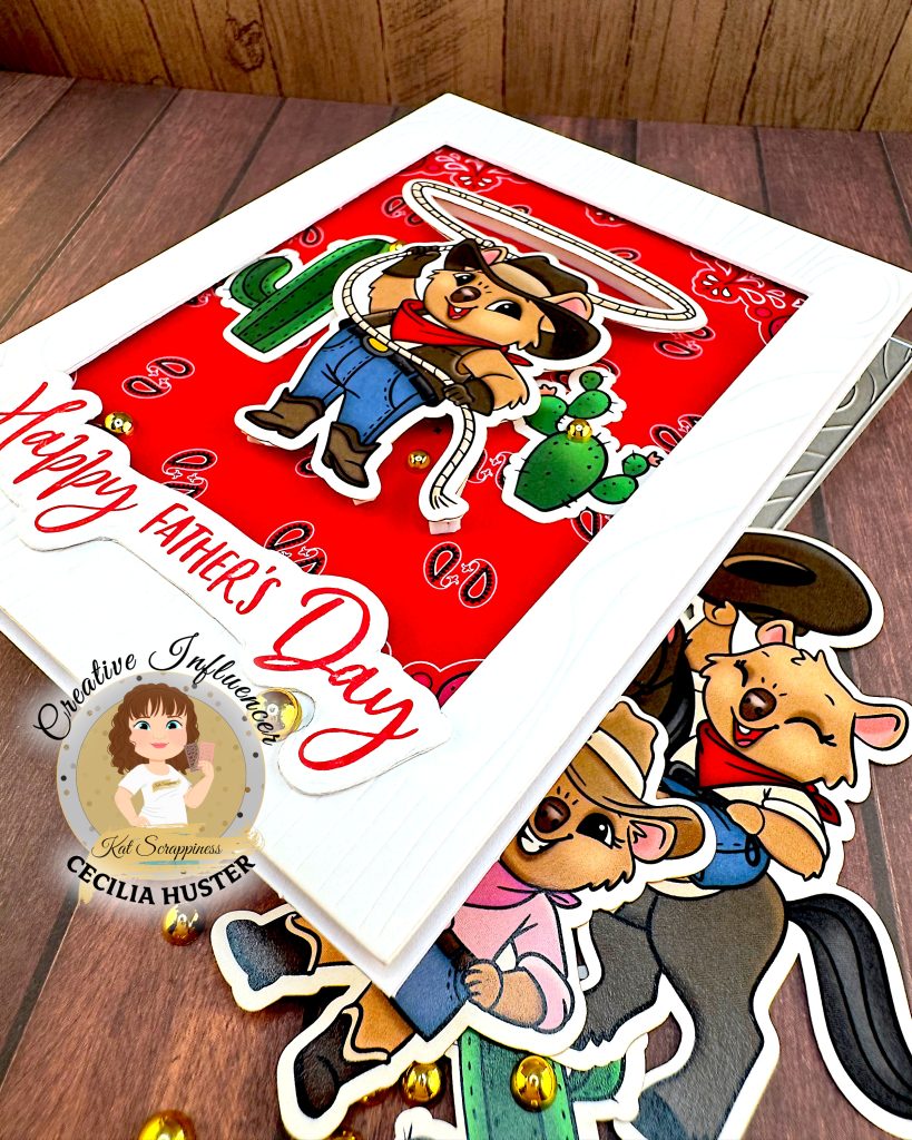 A Father's Day greeting card featuring a cute cartoon cowboy quokka character wearing a black cowboy hat, red bandana, and blue overalls. He is twirling a lasso with cacti in the background. The card has a red patterned background and "Happy Father's Day" text in red script lettering.
The scene is photographed at an angle from the bottom right on a wooden surface with cowboy-quokka-themed ephemera and gold beads.
There's a watermark for "Kat Scrappiness Creative Influencer CECILIA HUSTER" in the bottom left corner.