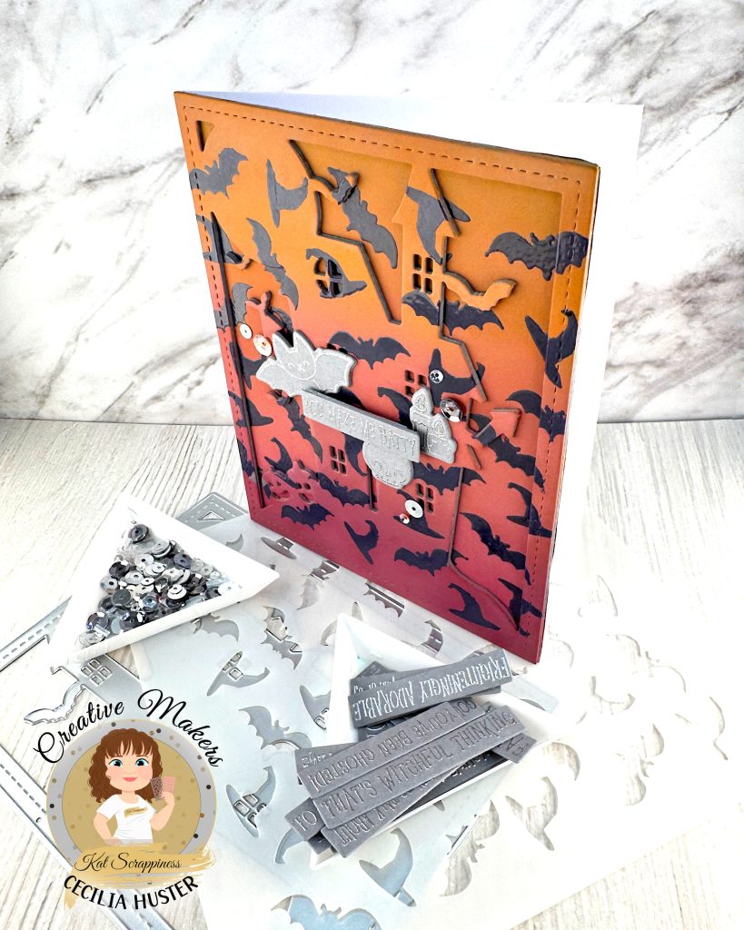 A handmade Halloween greeting card featuring an orange to dark pink gradient background filled with dark purple heat embossed bat silhouettes. The outline of a haunted mansion can also be seen.
The card has a decorative stitched border and contains silver embellished elements including a banner that reads "YOU MAKE ME BATTY." Around the sentiment a bat, a skull and some candles are grouped.
The card is photographed standing up and facing left on a white surface alongside metal cutting dies, sequins in a triangle tray, a stencil and other cardmaking supplies.
In the bottom left corner is a circular logo for "Creative Makers" featuring a cartoon woman with brown hair, credited to "Kat Scrappiness" and "CECILIA HUSTER."