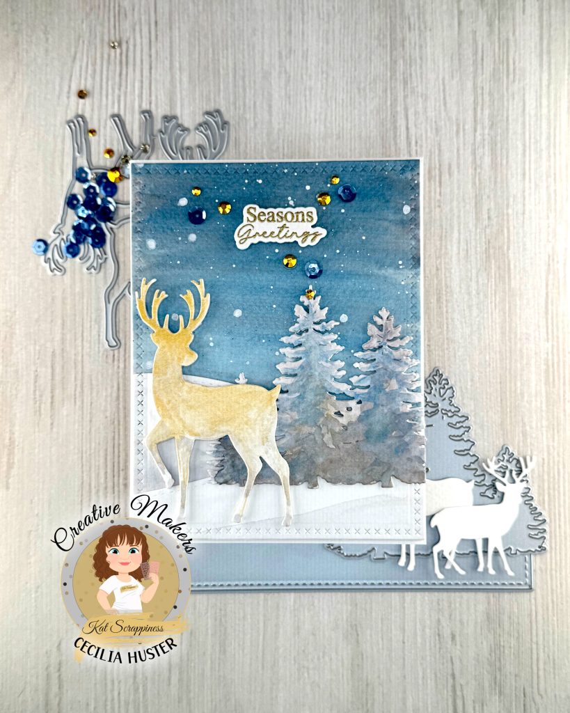 A handmade winter holiday card featuring a layered paper craft design. The card shows a watercolor winter scene with a golden deer silhouette standing in snow, surrounded by white pine trees against a blue starry sky. The text 'Seasons Greetings' appears at the top in gold lettering.
The card is decorated with blue and gold sequins scattered across the surface. On the left side are reindeer dies with blue sequins and gold rhinestones. The bottom right shows die-cut deer and tree silhouettes dies.
A circular logo in the bottom left identifies this as work by Kat Scrappiness designer Cecilia Huster, featuring a cartoon avatar of a woman with brown hair. The card is photographed against a white wood grain background.