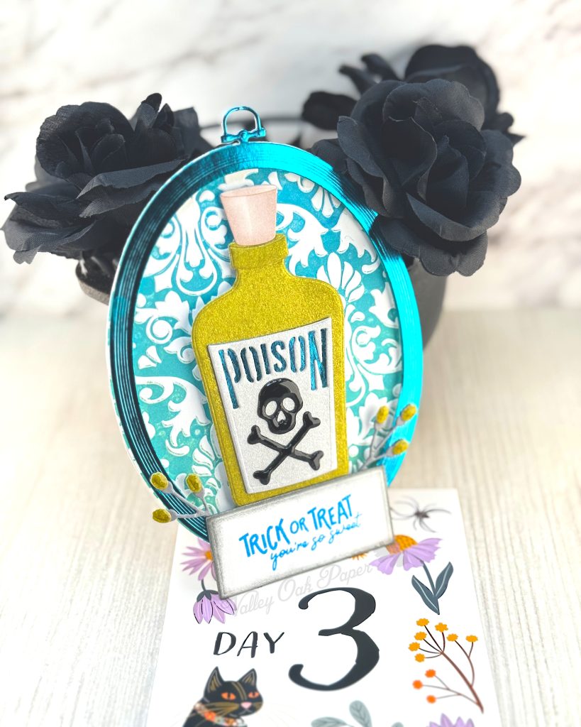 An oval greeting card with a damask background leans against a mini cauldron filled with black roses. 

The main feature of the card is a big green bottle with a poison label with a skull and crossbones.

The greeting reads "Trick or 
Treat, You're so Sweet."