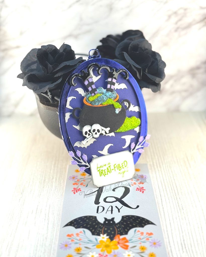 An oval greeting card leans against a mini cauldron filled with black roses. 

The main feature of the card is a large black cauldron. Something green and putrid is bubbling in the cauldron. Two pairs of witch's legs stick out of it. 

The background is purple with a pattern of witch's hats and bats. The greeting reads "Have a Treat-Filled Night."