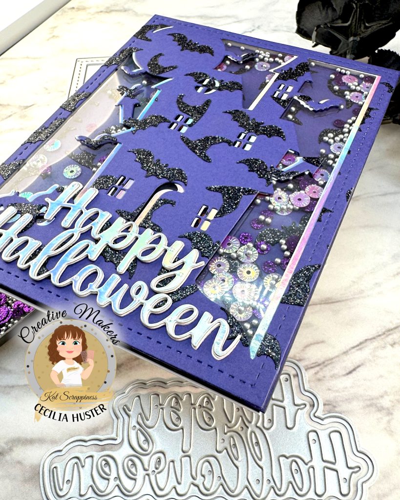 A close-up of a shaker greeting card in purple, black and silver is pictured against a white marble background. The card has an overall pattern of black glitter witchy hats and bats. The motif is a haunted house. Against the background we can see sequins in purple and silver tones. The silver sentiment reads Happy Halloween. This is a close-up of the lower right corner. 

The cover die, sentiment die and sequins that were used to create the card are also displayed. In addition, some black roses can be seen. In the lower left corner is a watermark that reads Creative Maker Cecilia Huster for Kat Scrappiness. 