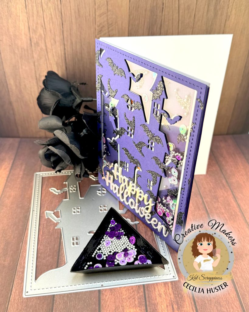 A shaker greeting card in purple, black and silver is pictured against a warm wood background. The card has an overall pattern of black glitter witchy hats and bats. The motif is a haunted house. Against the background we can see sequins in purple and silver tones. The silver sentiment reads Happy Halloween. The card faces left.

The cover die, sentiment die and sequins that were used to create the card are also displayed. In addition, some black roses can be seen. In the lower left corner is a watermark that reads Creative Maker Cecilia Huster for Kat Scrappiness. 