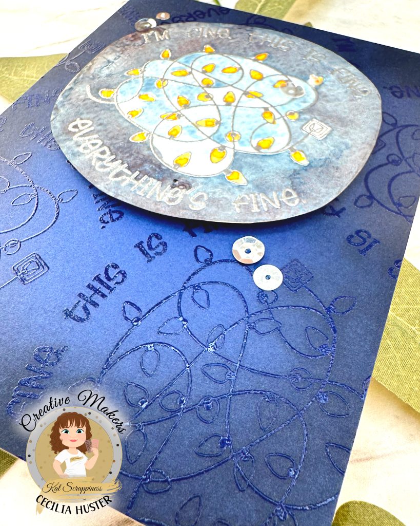 A handmade greeting card with a navy background. The main feature of the card is a watercolor panel showing a tangled light string with lights in amber.
The text around the image says "I'm fine. This is fine. Everything's fine." A few silver sequins adorn the card front.
The card has been photographed on a marble background with salvia leaves. The lower right corner is closest to the camera. This emphasizes the background pattern that repeats the main motif embossed with clear powder.
In the lower left corner is a watermark with the text "Creative Maker for Kat Scrappiness: Cecilia Huster."