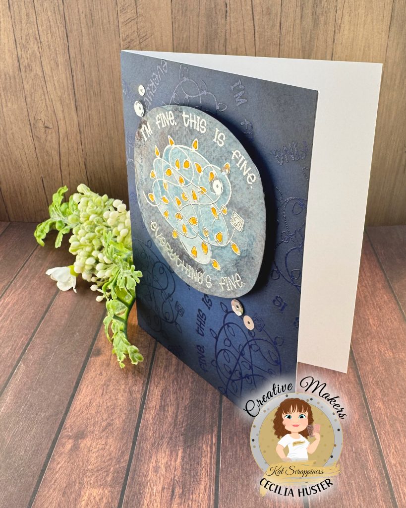 A handmade greeting card with a navy background. The main feature of the card is a watercolor panel showing a tangled light string with lights in amber.
The text around the image says "I'm fine. This is fine. Everything's fine." A few silver sequins adorn the card front.
The card has been photographed on a rustic wooden background. It's facing left. In the lower left corner is a watermark with the text "Creative Maker for Kat Scrappiness: Cecilia Huster."