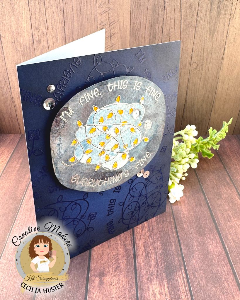 A handmade greeting card with a navy background. The main feature of the card is a watercolor panel showing a tangled light string with lights in amber.
The text around the image says "I'm fine. This is fine. Everything's fine." A few silver sequins adorn the card front.
The card has been photographed on a rustic wooden background. It's facing right. In the lower left corner is a watermark with the text "Creative Maker for Kat Scrappiness: Cecilia Huster."
