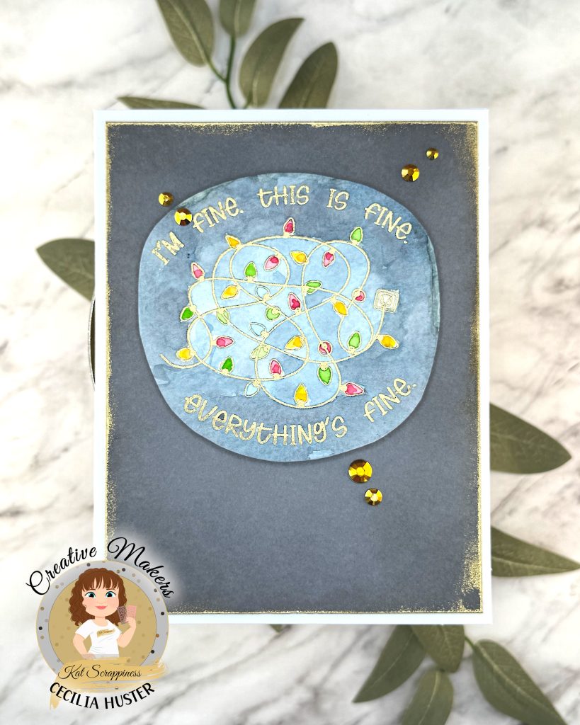 A handmade greeting card with a grey background outlined in grungy gold. The main feature of the card is a watercolor panel showing a tangled light string with lights in red, amber and green.
The text around the image says "I'm fine. This is fine. Everything's fine." A few gold gems adorn the card front.
It's photographed on a marble background on top of sage leaves. In the lower left corner is a watermark with the text "Creative Maker for Kat Scrappiness: Cecilia Huster."