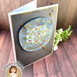 A handmade greeting card with a grey background outlined in grungy gold. The main feature of the card is a watercolor panel showing a tangled light string with lights in red, amber and green. The text around the image says "I'm fine. This is fine. Everything's fine." A few gold gems adorn the card front. It's photographed on a rustic wooden background. In the lower left corner is a watermark with the text "Creative Maker for Kat Scrappiness: Cecilia Huster."