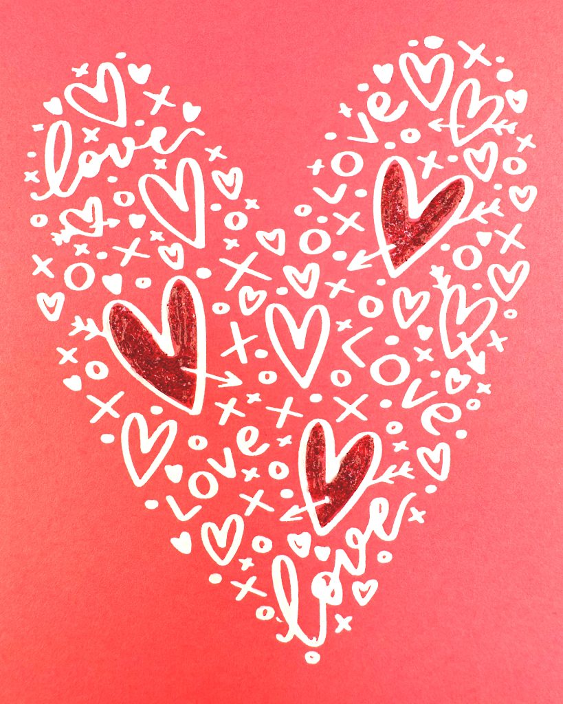 A closeup of a heart shape that consists of white hearts, x's and o's as well as the word love. Three of the largest hearts have been filled in with red glitter glue. The background is a lovely coral color.